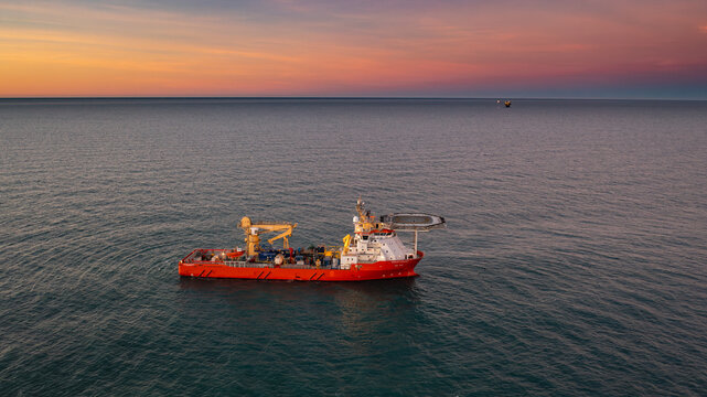 Aerial view of a supply vessel navigating the Magellan Strait at sunset with an oil rig visible in the distance in Santa Cruz, Argentina.