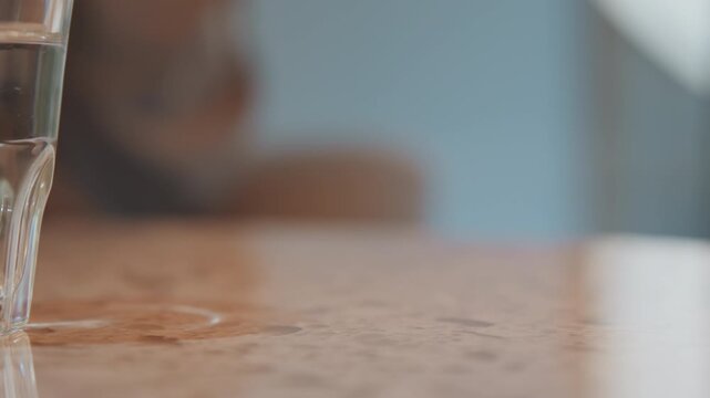 Close up of brown leather wallet on wooden table with soft lighting. hand rests near wallet indicating interaction or presence. Glass object visible in background suggesting casual indoor