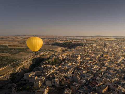 Aerial view of a yellow hot air balloon floating over the historic stone buildings and narrow streets of Gravina in Puglia, Apulia, Italy.