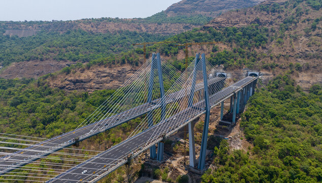 Aerial view of the Atal Setu cable-stayed bridge spanning a lush green valley with mountain slopes and tunnel entrances in Lonavala, Maharashtra, India.
