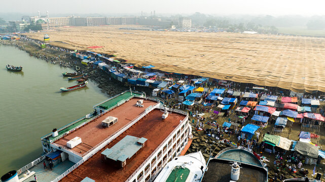 Aerial view of the Charmonai Mahfil gathering with colorful tents, boats docked along the riverbank, and a large canopy covering the event area in Charmonai, Barisal Division, Bangladesh.