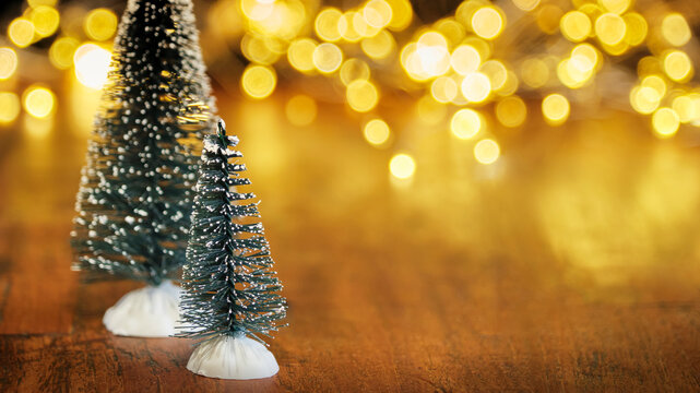 Christmas or New Year greeting card template with snow covered miniature Christmas trees and Christmas lights in the background. Xmas holidays atmosphere. Image with copy space and selective focus.	