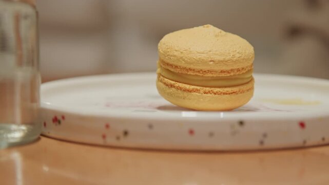 Close up of yellow macaron on white plate with colorful dots placed centrally. scene remains static without any movement or change in composition focusing solely on stationary dessert