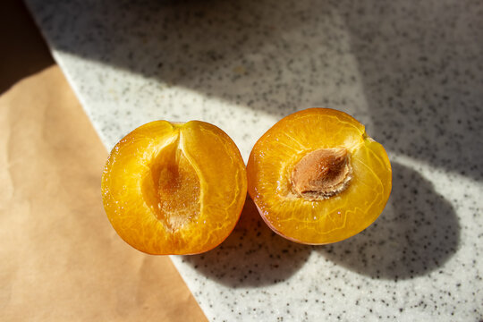 Fresh ripe plum cut in half showing yellow juicy flesh macro. Sweet mirabelle or greengage plum stone fruit with seed pit on stone table under bright sun, healthy organic superfood background.