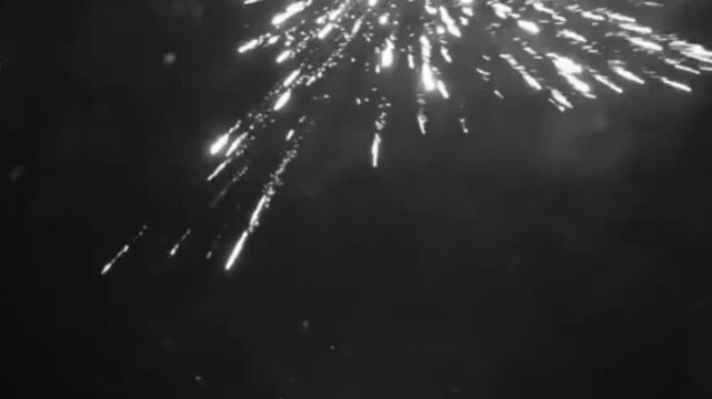 Dramatic black and white image of fireworks exploding in a night sky with bright sparkling trails