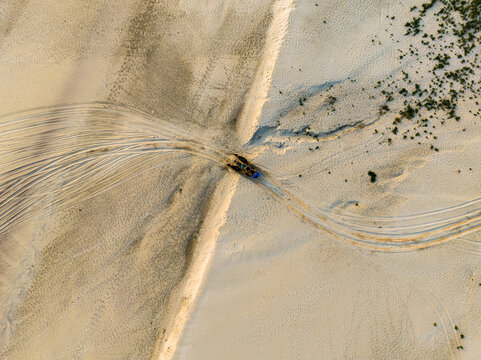 Aerial view of tire tracks across sandy terrain with a small vehicle moving through the landscape in Rajshahi, Rajshahi Division, Bangladesh.