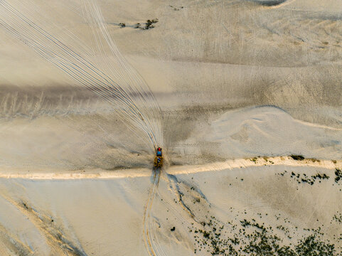 Aerial view of a vehicle driving through a sandy landscape with visible tire tracks stretching across the terrain in Rajshahi, Rajshahi Division, Bangladesh.