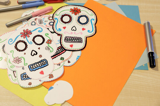 Colorful handmade paper skulls arranged with craft supplies for Day of the Dead