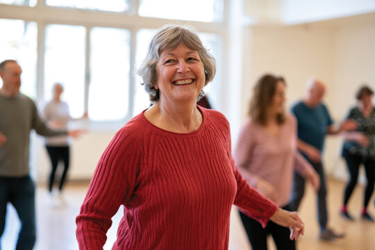 An older woman smiles brightly while dancing in a group class, highlighting the joy and vitality of movement and connection among participants of various ages.