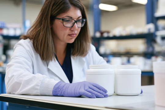 A focused female scientist in a laboratory setting examines three white containers, showcasing care and precision in chemical analysis or research processes.