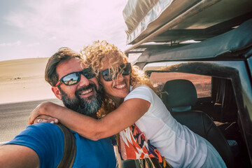 Smiling man and woman hugging, traveling in an off-road vehicle during a desert road trip,...