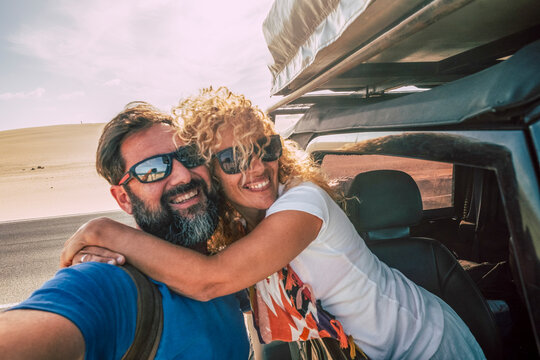 Smiling man and woman hugging, traveling in an off-road vehicle during a desert road trip, experiencing freedom and happiness on their summer vacation