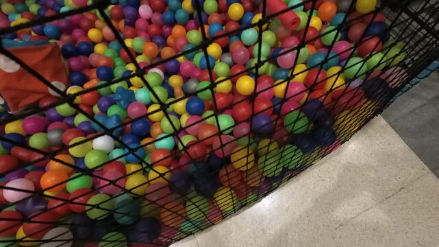 Many colorful plastic balls in a children's playground ball pit moving and shaking behind a net