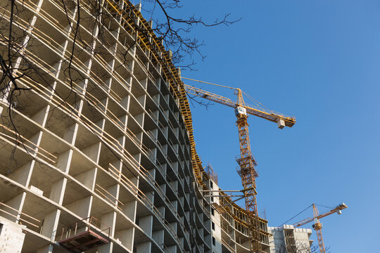 Monolithic concrete frame of unfinished curved building with tower crane on construction site