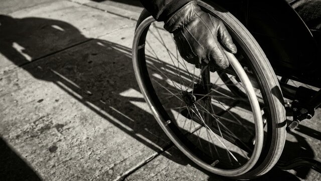 Disability - Gloved Hand Gripping Wheelchair Rim on Sunlit Concrete Sidewalk in Black and White