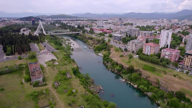Morača River crossing central Podgorica beside modern millenium bridge and urban districts in Montenegro, aerial