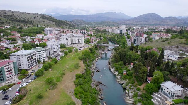 Morača River flowing through Podgorica urban districts toward surrounding mountains, aerial establishing dolly backdrop