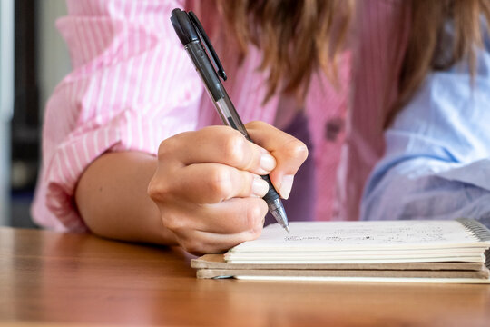 Woman's hand holding a pen, writing notes and ideas in a spiral notebook on a desk, symbolizing study, planning, creativity, organization and professional or student work