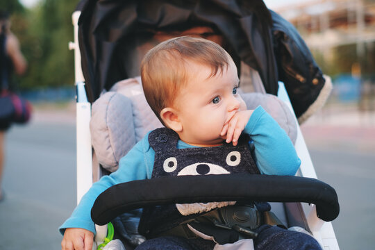 Cute baby boy sitting in stroller outdoors with hand in mouth stock photo