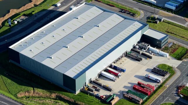 Cinematic drone flight over vast iPort logistics warehouses and rail freight interchange bathed in warm golden hour light