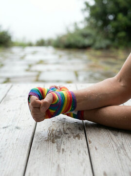 Hand wrapped in rainbow tape resting on grey dock planks by water outdoors