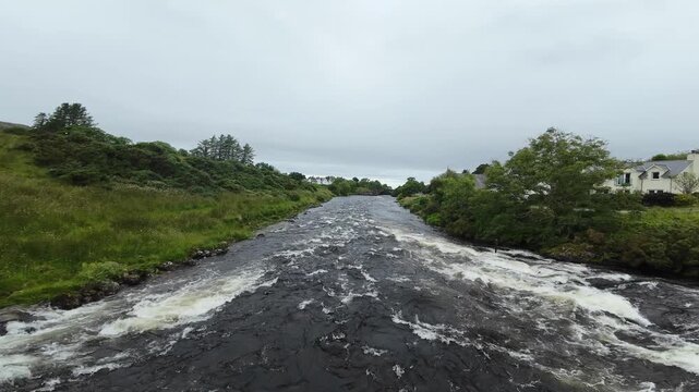 FPV drone flight over the river Ewe. Shot in Poolewe in the Highlands of Scotland the flight follows the course of the river through a typical village setting. The flight approaches a road bridge.