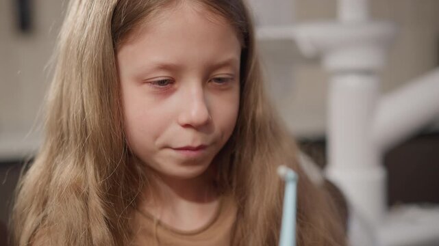 Close up of young girl with long blonde hair examining orthodontic retainer in soft indoor lighting. scene focuses on her interaction with dental appliance highlighting details like texture