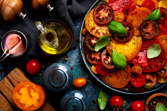 Organic tomato salad, homemade vegan vegetable dish with fresh basil on dark background. Seasonal local farmers market harvest and raw diet concept. Natural plant based wholesome food recipe flat lay.