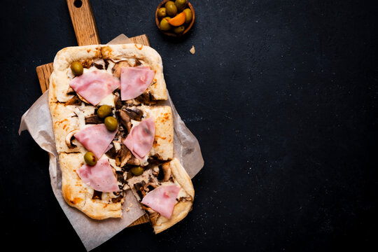 Hot baked pizza with juicy ham, cut mushroom and olive atop rustic wooden board. Social gathering shared meal and comfort food enjoyment. Genuine italian culinary heritage recipe.