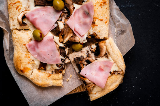 italian food - pizza slice with mushroom, ham, melted cheese and green olives. Satiety and food craving satisfaction concept. Delicious culinary masterpiece on wooden board.