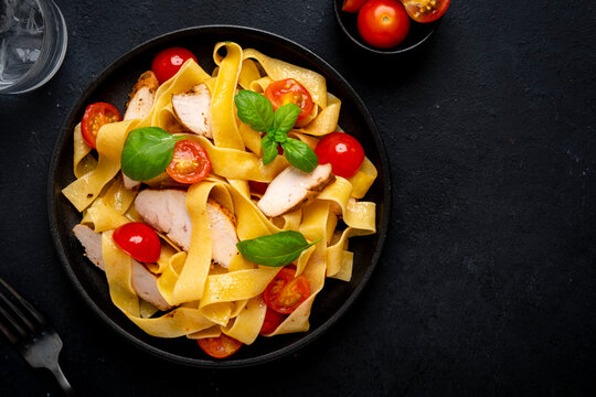 Traditional pasta topped with tender chicken and green basil. Freshness and comfort food serving idea. Prepared appetizing lunch portion waiting on wooden table next to glass of cold water.