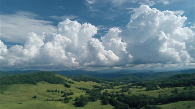 Vast Aerial Landscape of Rolling Green Hills and Mountains under a Dramatic Sky with Large Cumulus Clouds