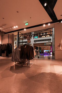Warsaw, Poland, 20 August 2026. Clothing store inside a modern shopping mall, showing racks of fashion items and an exit to the main concourse