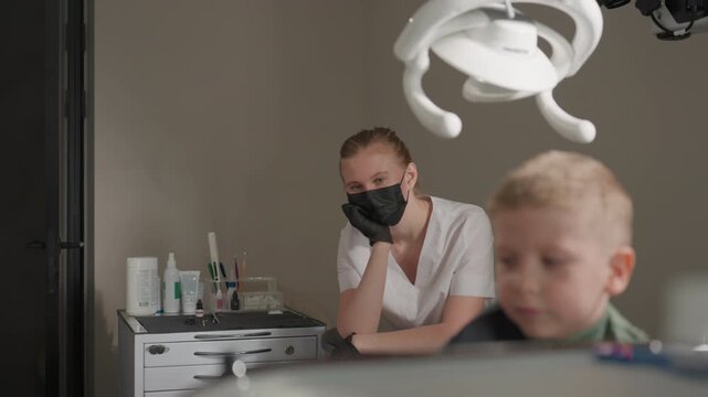 Close up of dental professionals in clinical setting observing and preparing for orthodontic treatment. woman wearing black glasses stands near another woman seated at workstation