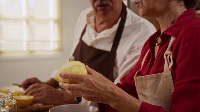 Caucasian middle aged woman peeling citrus zest beside senior man during cooking. Footage fitting for culinary workshops, home recipe tutorials, and family wellness campaigns