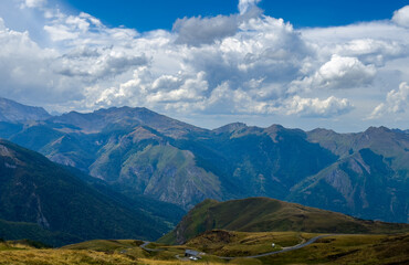Fototapeta premium serene mountain range overlooking the valley with a road and clouds in a natural outdoor setting, high vantage point, travel adventure nature theme, green and blue tones.