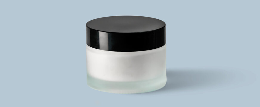 Frosted glass cosmetic jar with black lid and cream on pale blue background