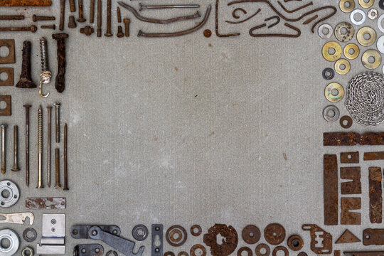 A frame of various old rusty bits and pieces arranged on a concrete surface. Old rusty nuts, bolts, nails and other parts flay lay on gray background.