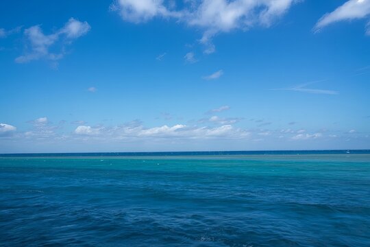 Vast expanse of deep blue ocean water meeting a clear sky with scattered white clouds on the horizon under bright daylight in a tropical coastal landscape with calm waves and deep sea colors