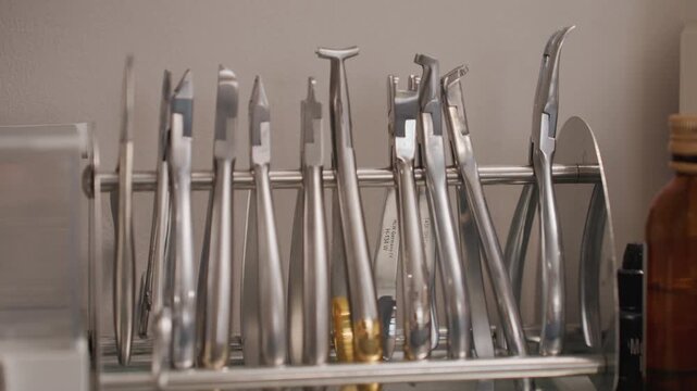 Close up of various dental instruments arranged in metal rack showcasing different shapes and sizes. tools are made of polished stainless steel with some featuring golden tips or unique
