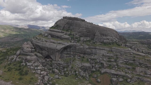 4K 30fps aerial rise toward a massive rounded rock with green trees on top. Shot in a flat color profile, ideal for professional color grading and LUT application.