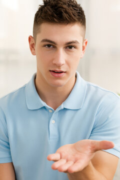 A young handsome guy in a blue polo shirt shows an open palm, you can insert the advertised item.