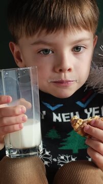 Vertical video. Small boy drinking milk and eating cookies at Christmas. Cozy festive mood