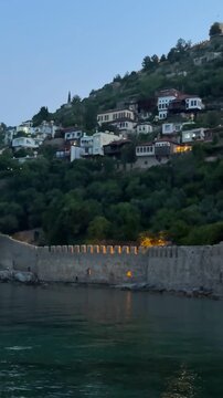 Illuminated ancient Tersane shipyard in Alanya with lights and houses on the hill of the historical peninsula at dusk