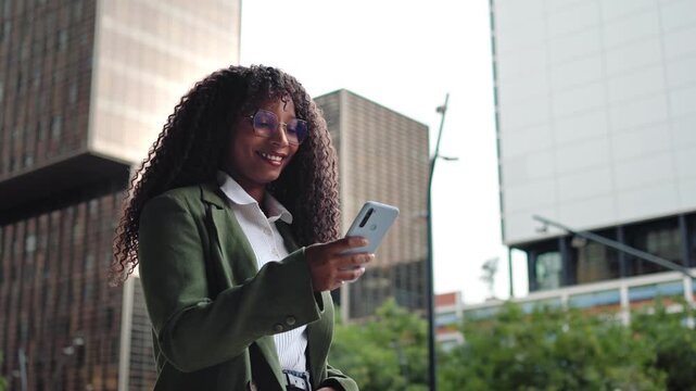 Young elegant African American Woman walking Using Smartphone In Modern Business District