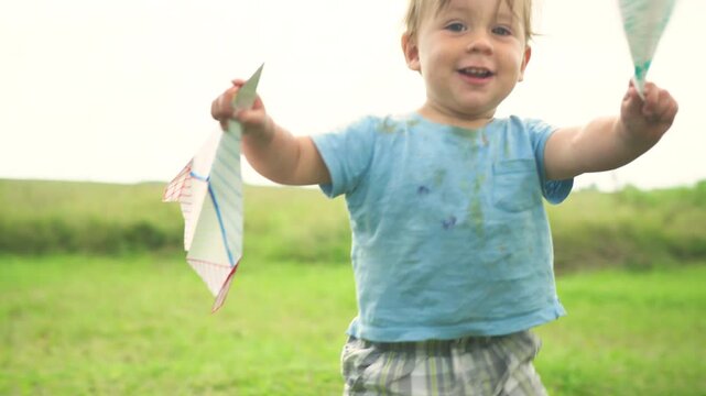 Little toddler playing in a field with paper airplanes on a sunny day