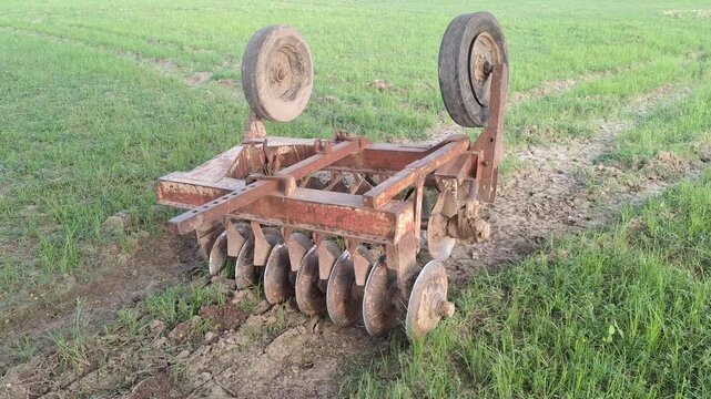 Agricultural disc harrow machine parked on a green rural farm field for secondary tillage soil preparation