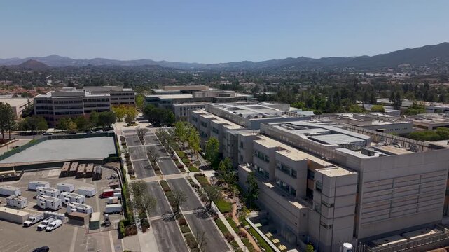 Expansive drone video reveals Amgen&rsquo;s corporate headquarters in Thousand Oaks, California, with modern office buildings, wide streets, and distant mountain views under clear daylight skies.