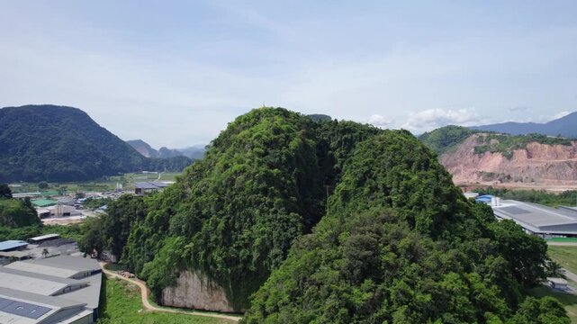 Aerial drone flight past a golden Buddhist stupa on a forested karst mountain, revealing dramatic limestone formations and a vast tropical landscape in Malaysia.