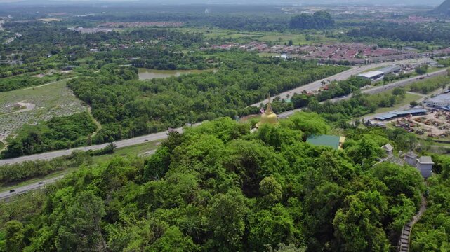 Scenic aerial perspective of a mountaintop Buddhist stupa overlooking a highway and sprawling development, contrasting a spiritual landmark with modern infrastructure.